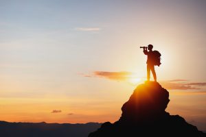 vision for success ideas. businessman's perspective for future planning. Silhouette of man holding binoculars on mountain peak against bright sunlight sky background.